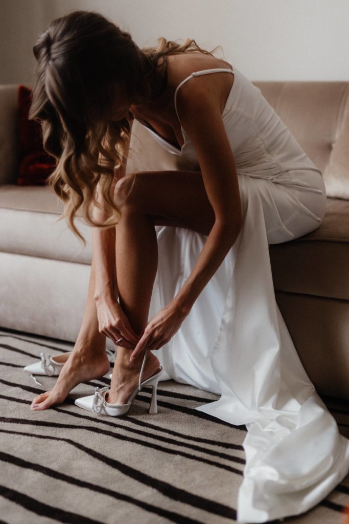 A bride tying her shoes on a couch.