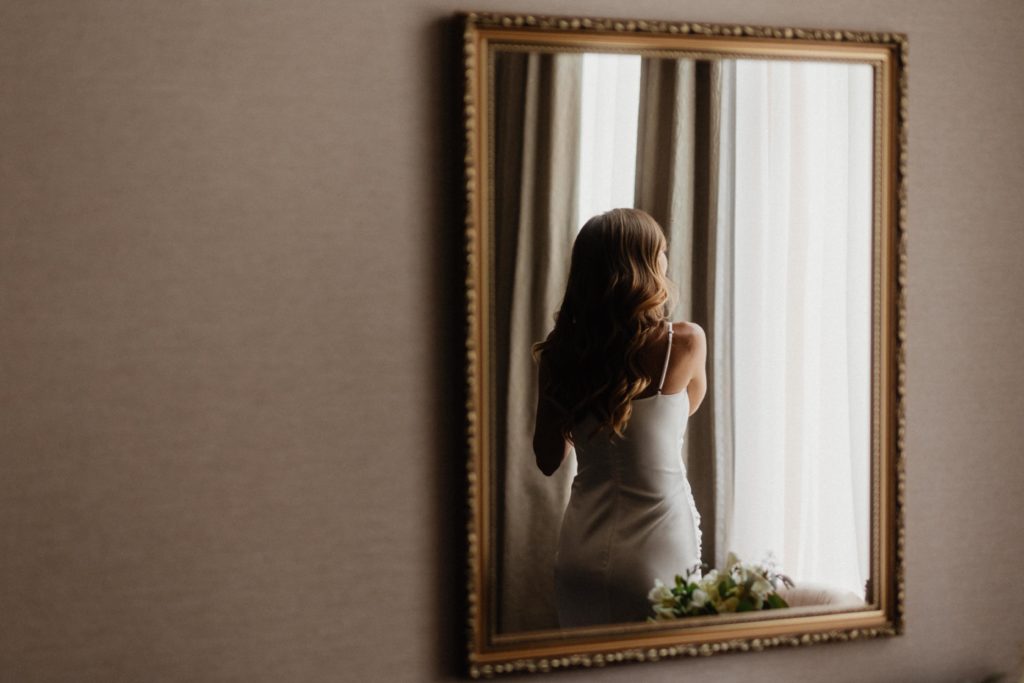 A bride in a wedding dress looking at herself in a mirror.