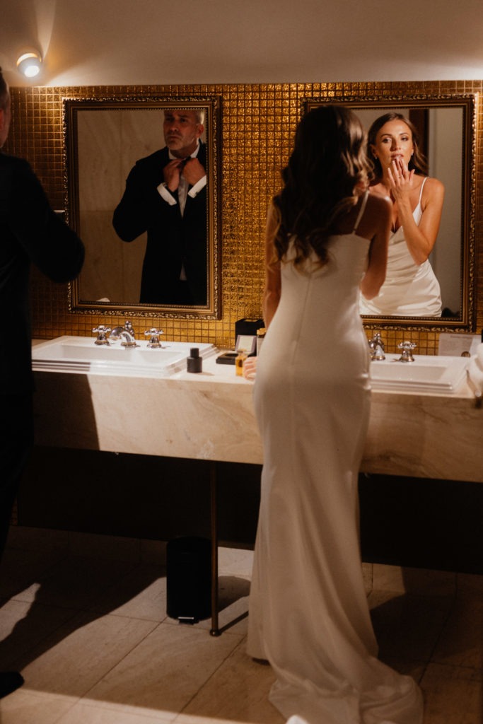 A bride and groom getting ready in a bathroom.