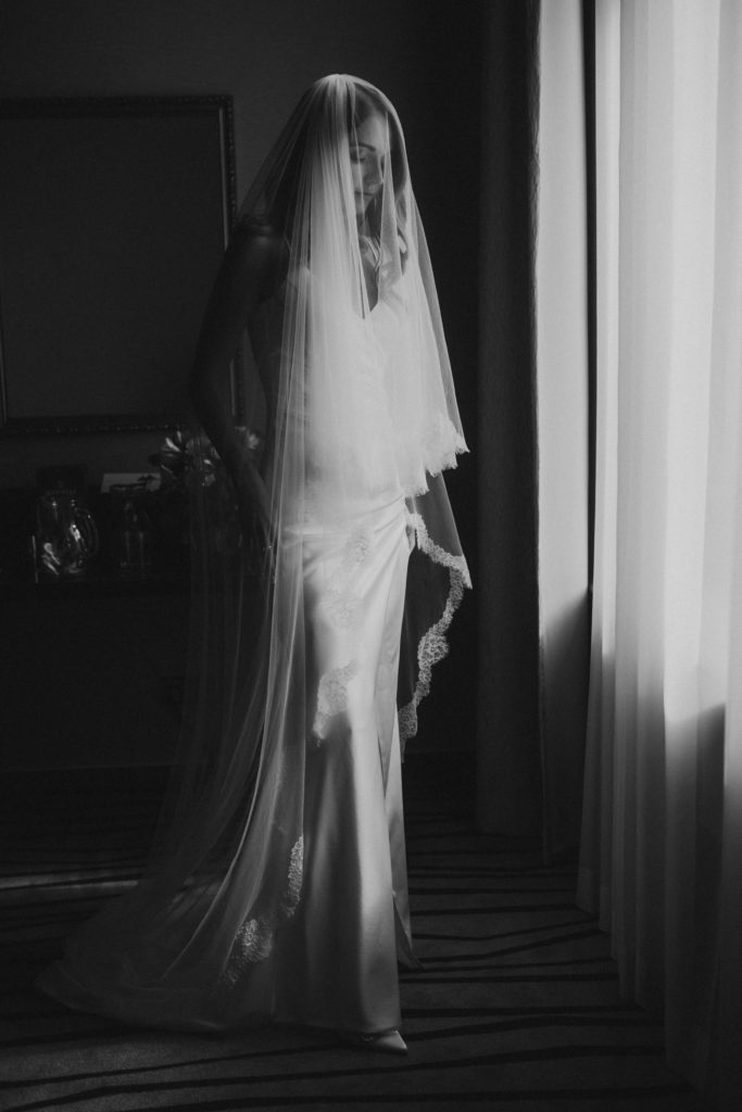 A bride wearing a veil in front of a window.