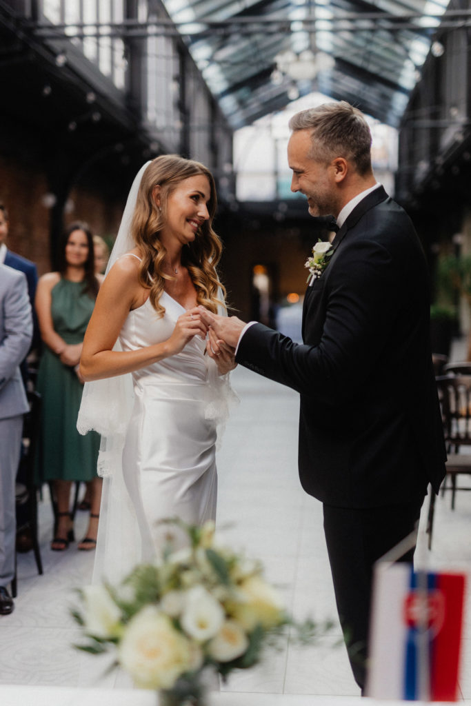 A bride and groom exchanging rings in a courtyard.