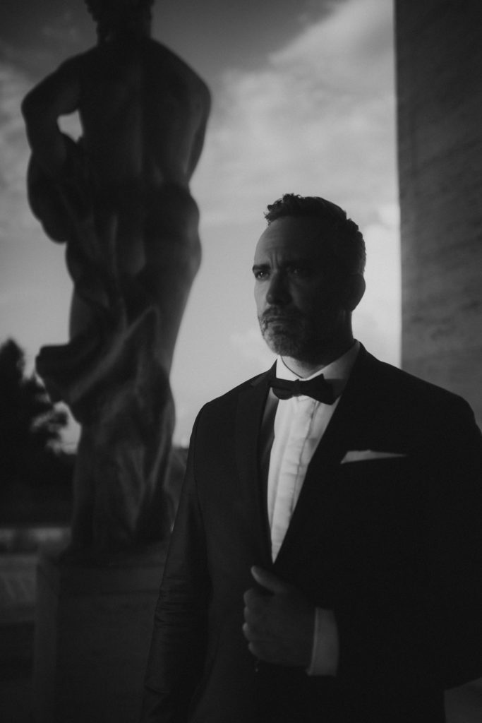 Stylish groom standing in front of minimalism architecture in Rome