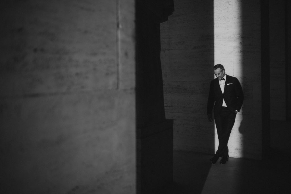 Stylish groom standing in front of minimalism architecture in Rome