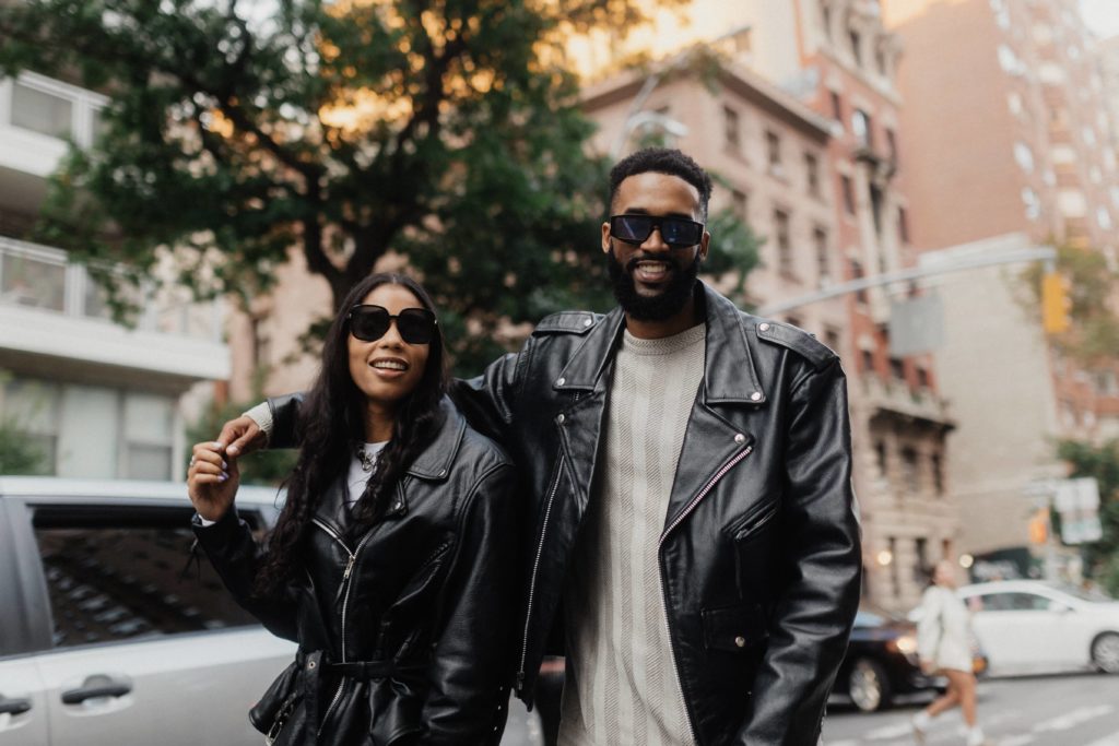 A black couple in leather jackets standing on a city street.