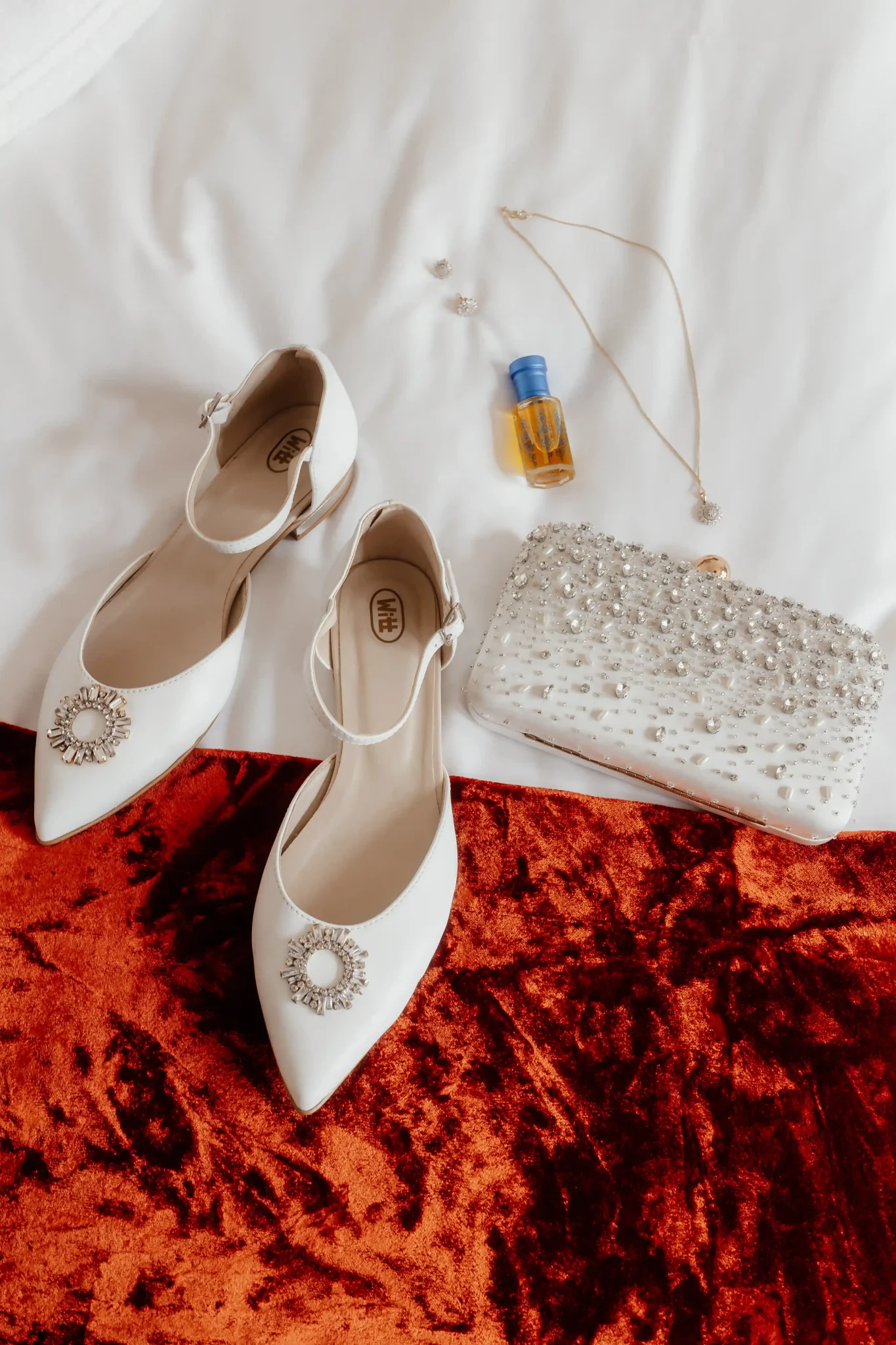 A white pair of shoes and a clutch on a bed.