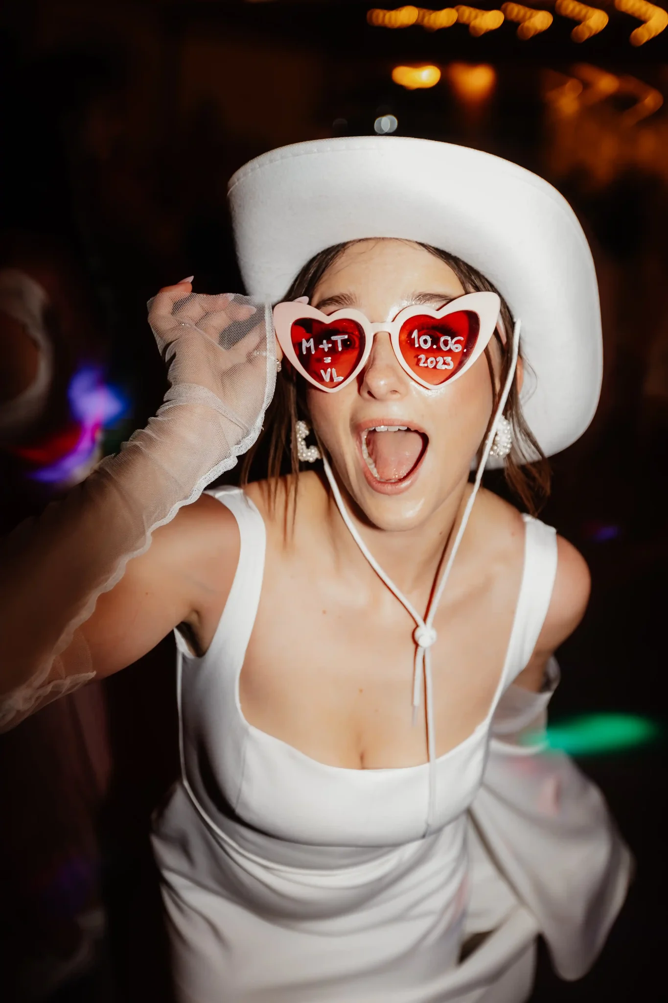 A woman in a white dress and hat is wearing sunglasses.