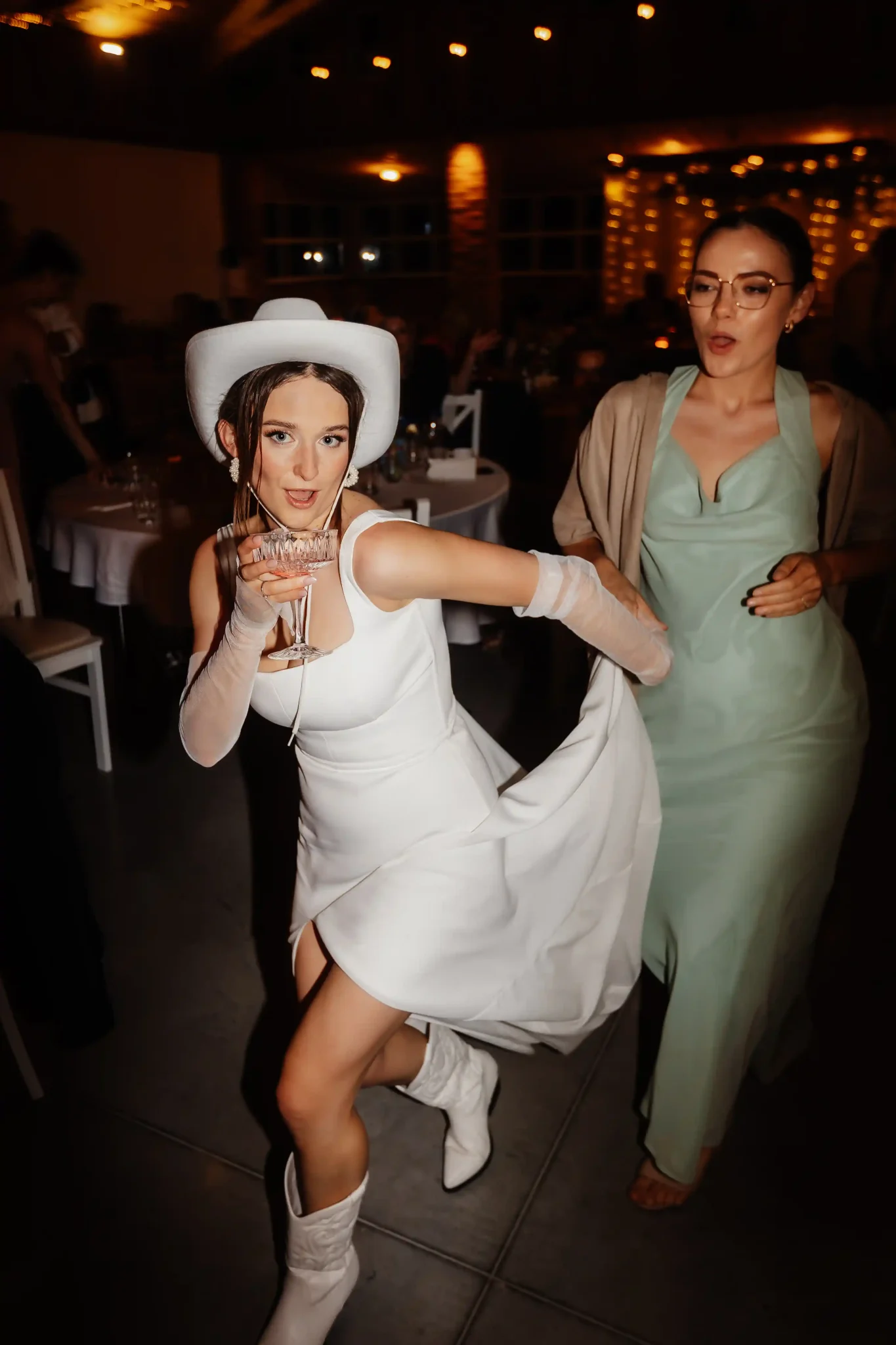 A woman in a white dress dancing with a woman in a cowboy hat.