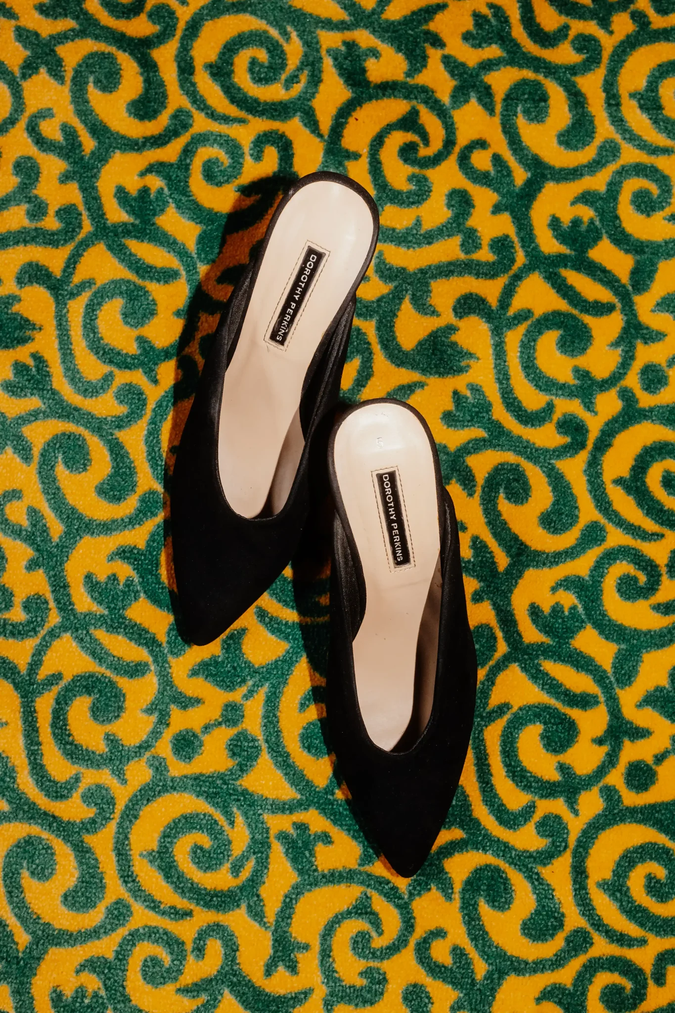 A pair of black shoes on a yellow and green carpet.