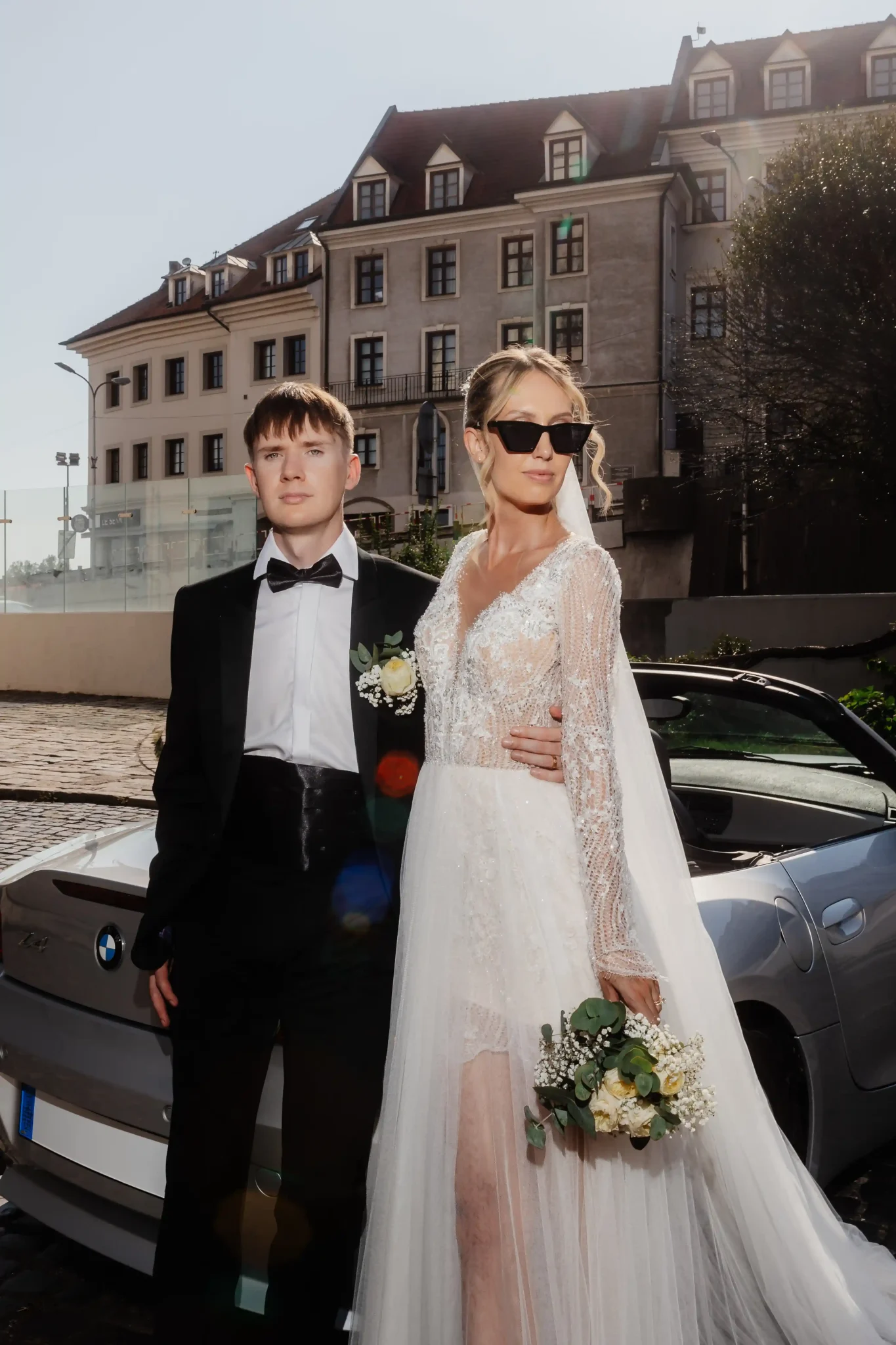 A bride and groom standing next to a bmw sports car.