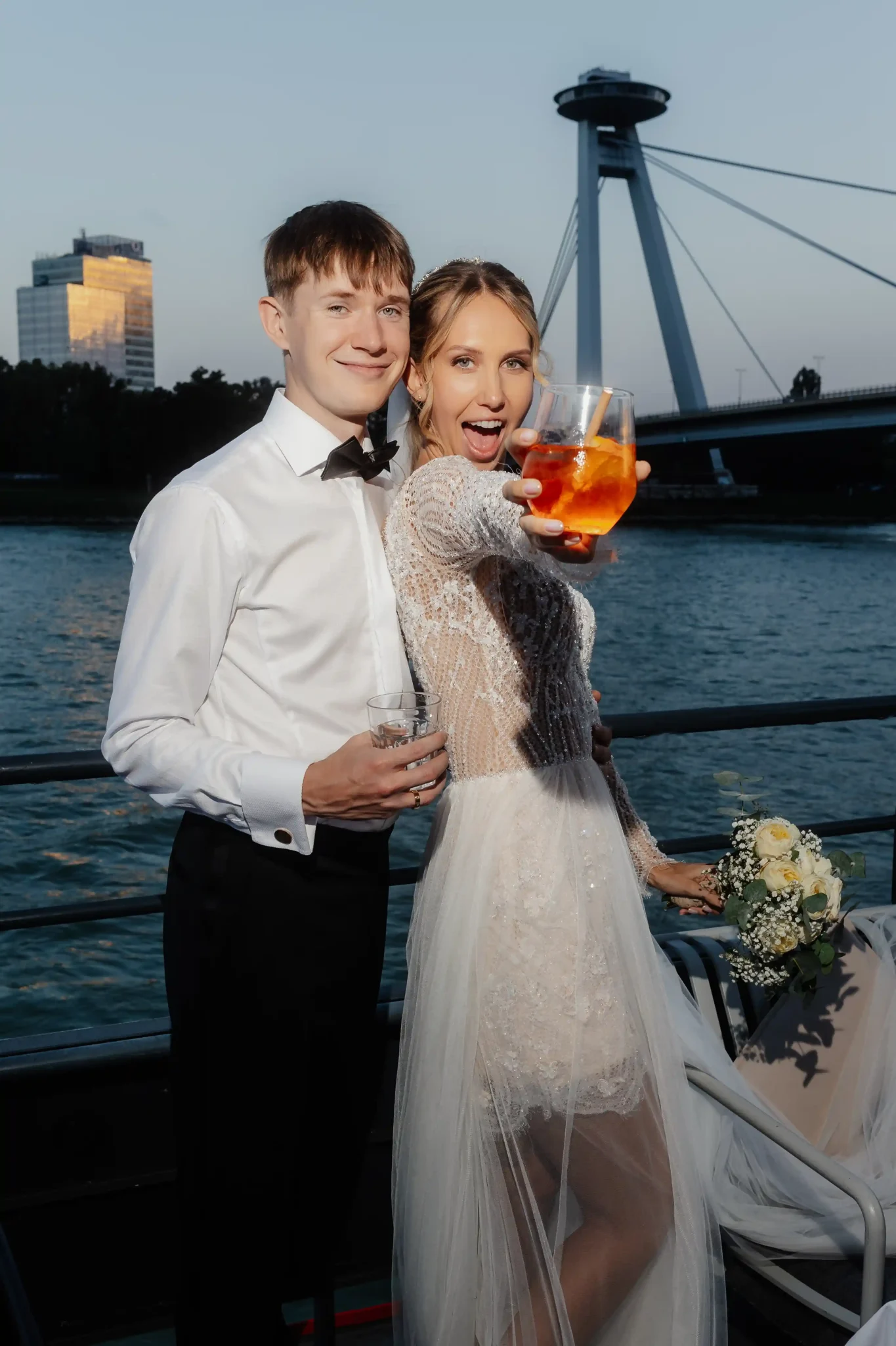 A bride and groom pose for a photo on a boat.