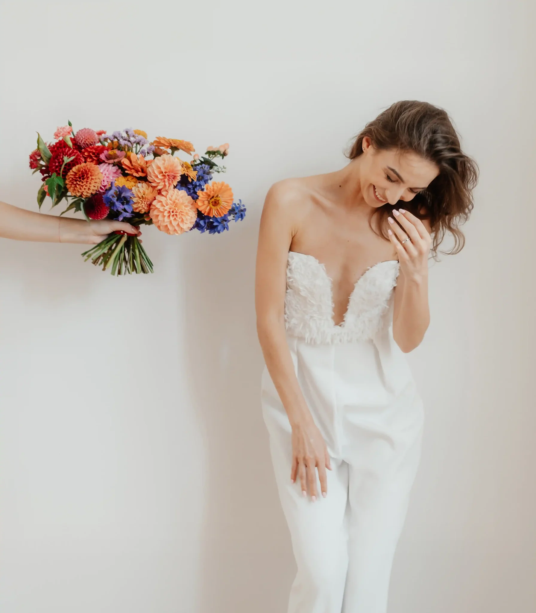 A bride in a white jumpsuit holding a bouquet of flowers.