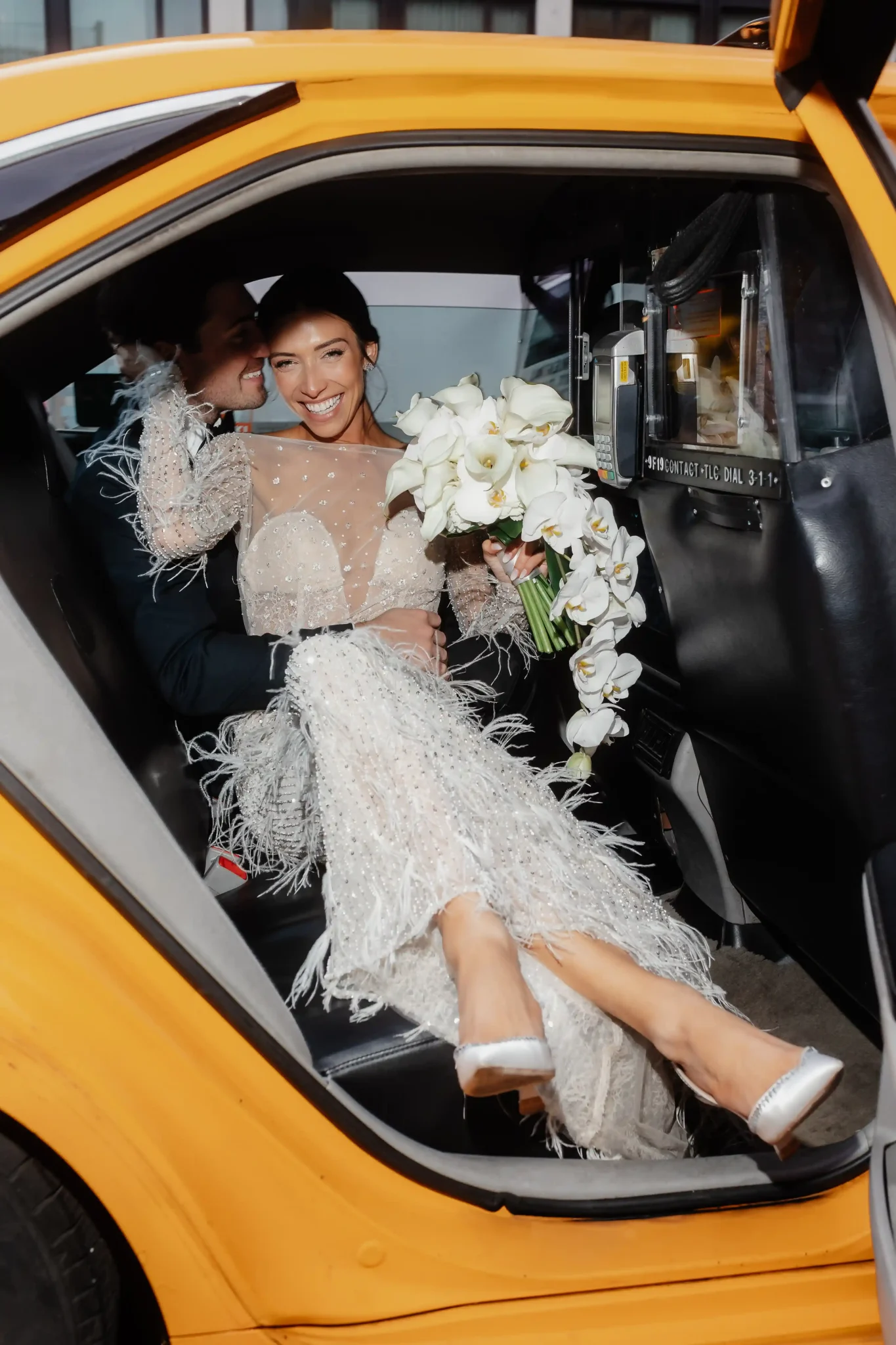 A bride and groom sitting in the back seat of a yellow cab.