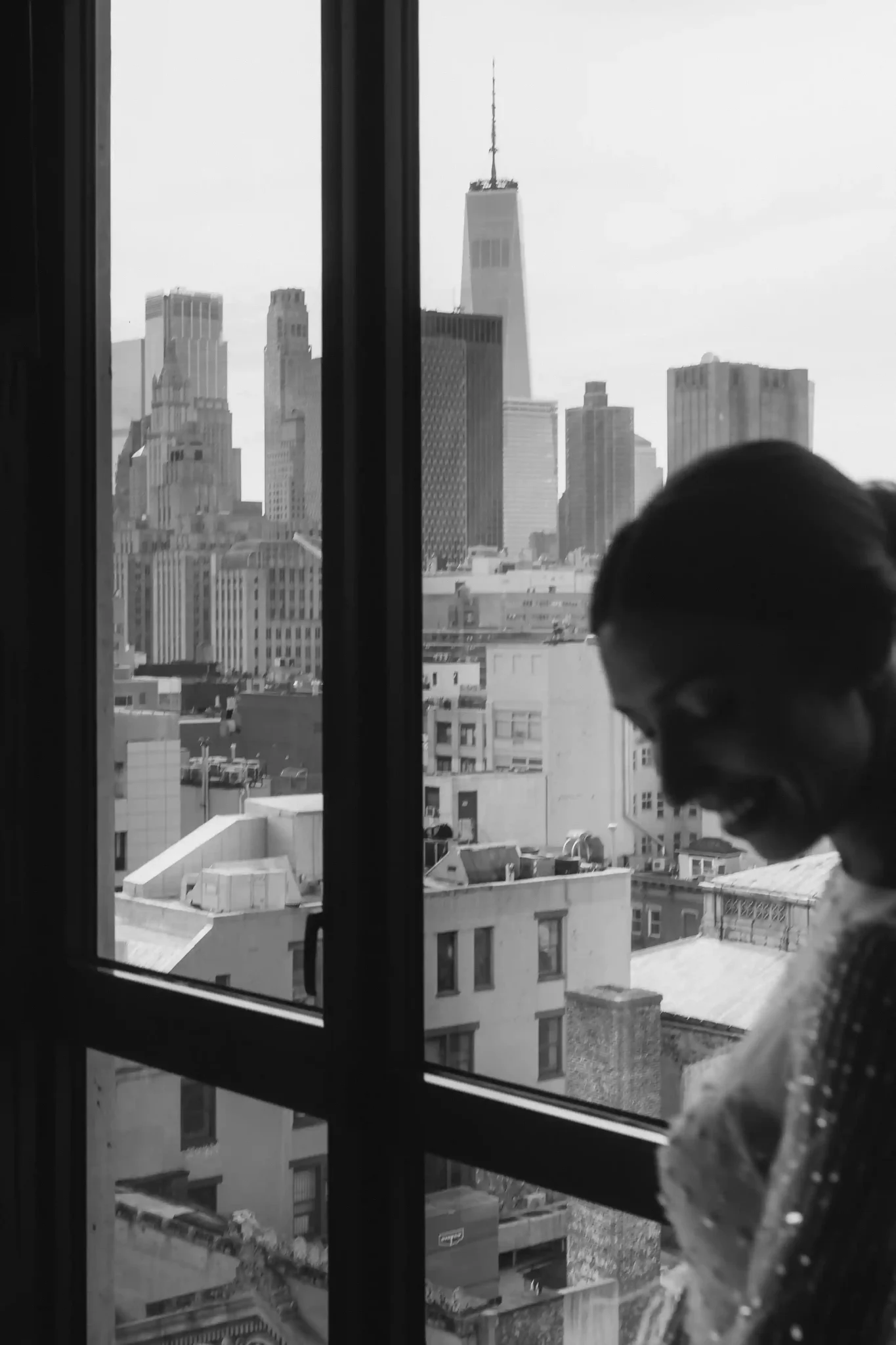 A bride looking out of a window with a view of the city.