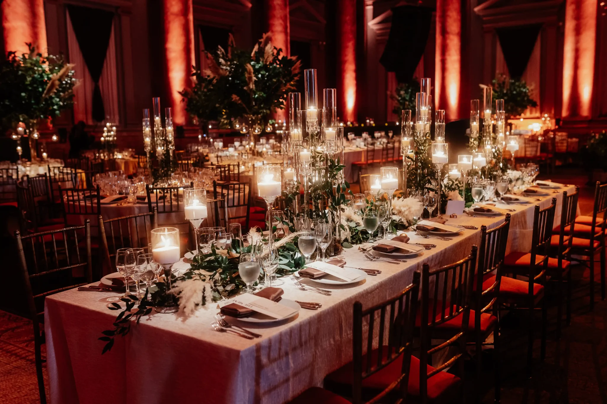 A long table with candles and greenery in a large room.