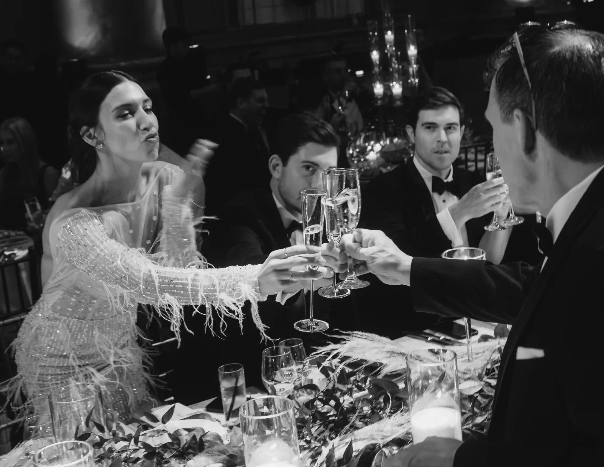 A black and white photo of people toasting at a dinner table.