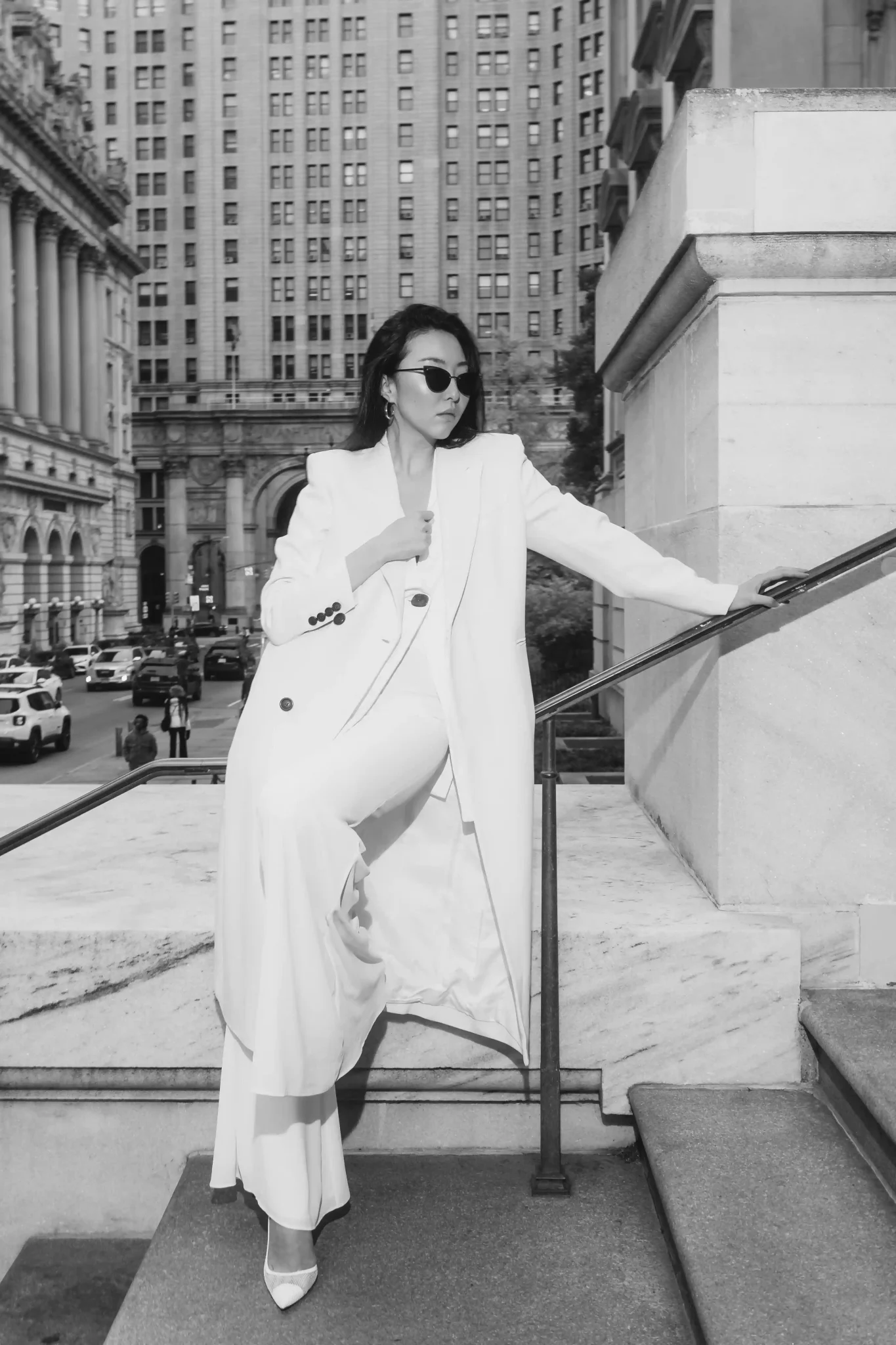 A woman in a white coat posing on the steps of a building.